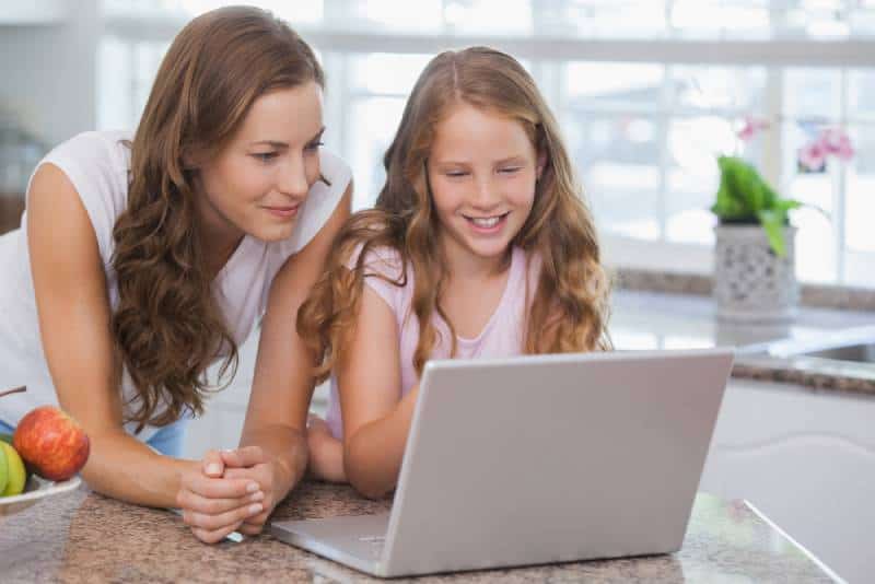 smiling girl and mother using laptop in the house