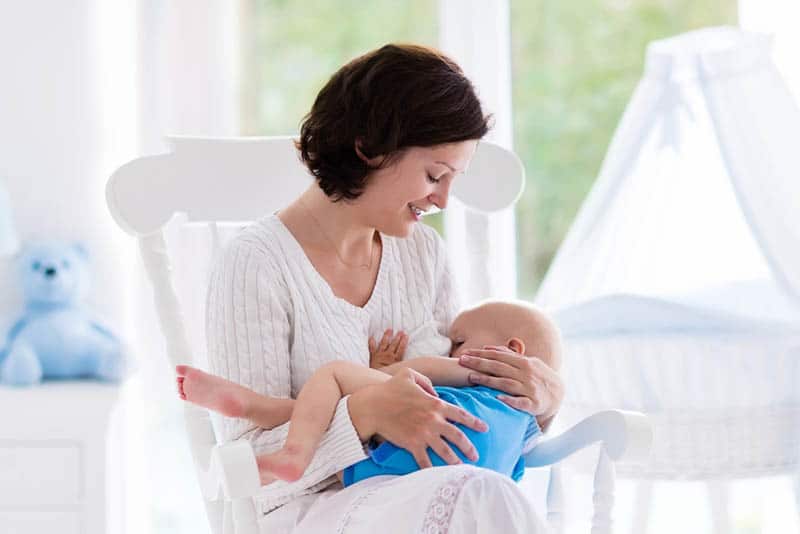 woman sitting on bed and breastfeeding her baby