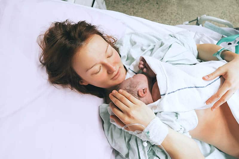 young woman holding her newborn baby in arms in hospital bed 