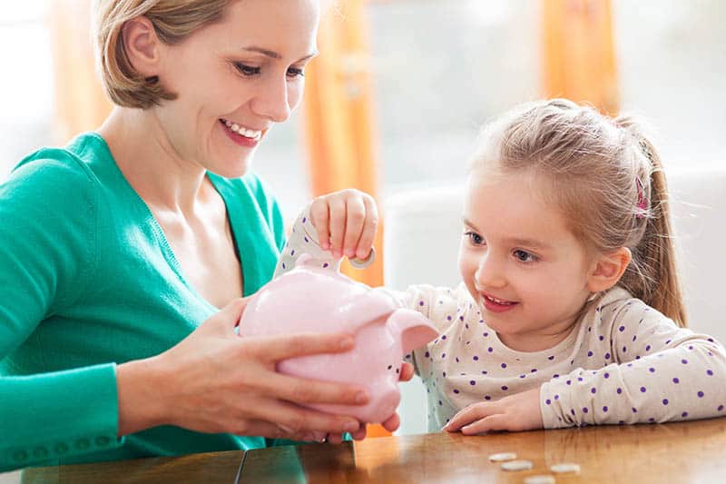 Woman holding piggy bank and daughter putting money in it