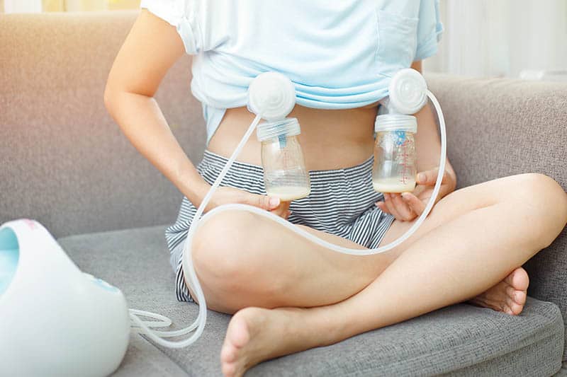 Woman is pumping breast milk while sitting on a sofa