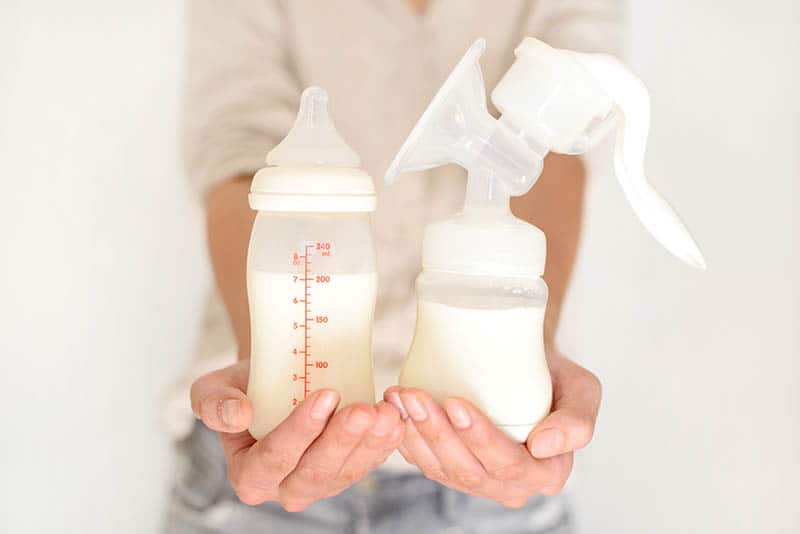 woman holding breast milk in a bottle along with the manual breast pump