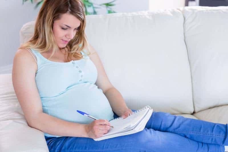 pregnant woman writing down notes in a notebook