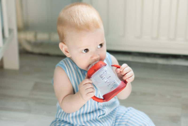 Baby boy drinking from baby cup and sitting on floor