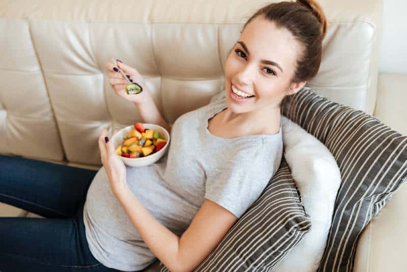 smiling pregnant woman eating a fruit salad