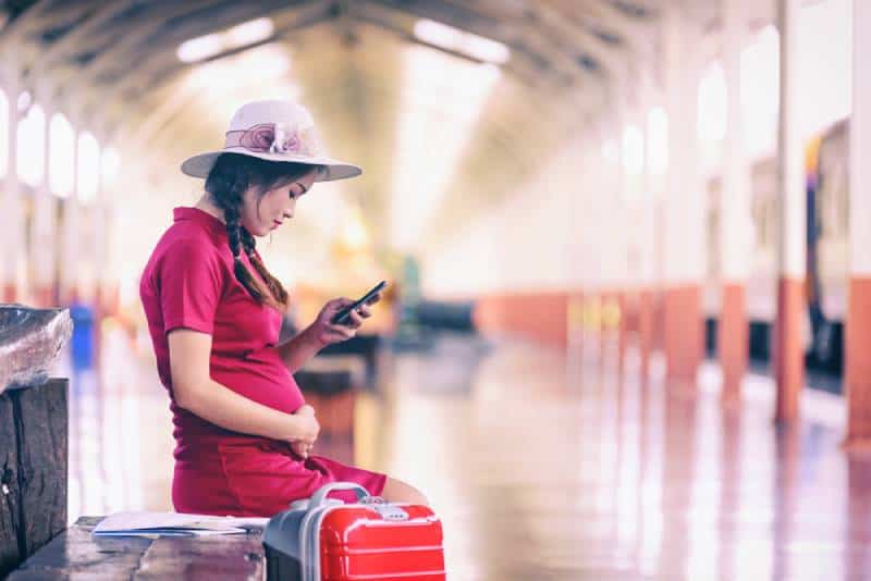 Pregnant woman with a suitcase waiting for the train