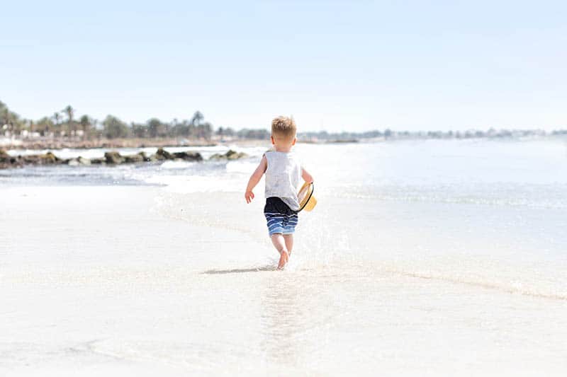 Little boy walking on the beach holding a hat