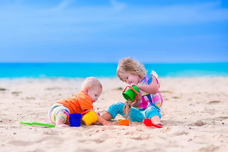 Toddler and a baby playing with sand