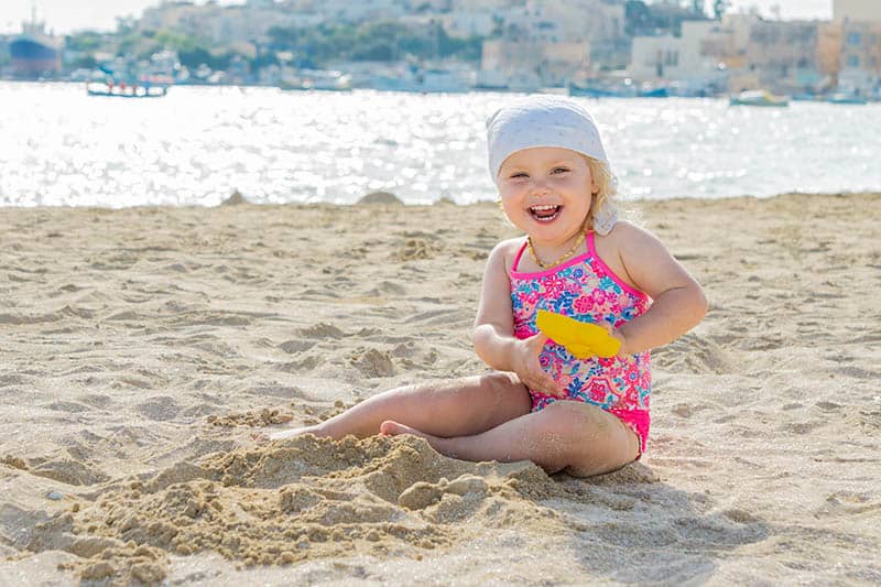 Little happy girl sitting on the beach