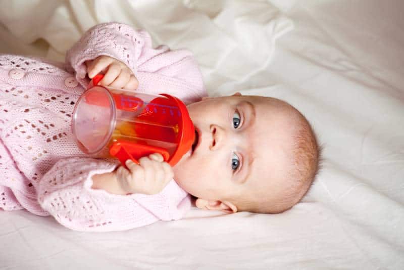 baby girl with sippy cup lying on blanket