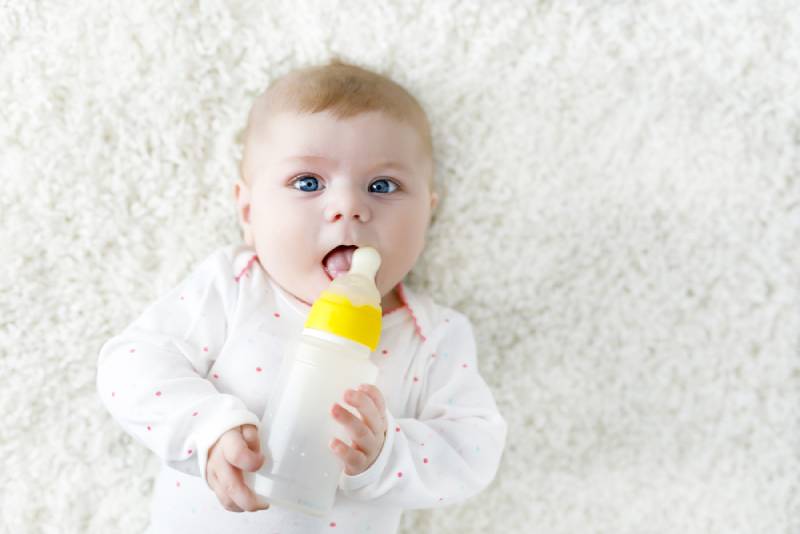 Baby holding nursing bottle and drinking formula milk