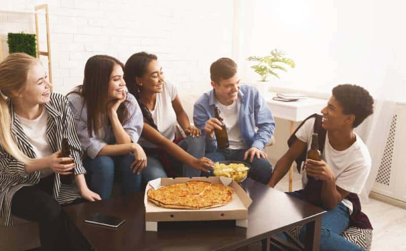 Group of teenagers eating pizza and chatting at home