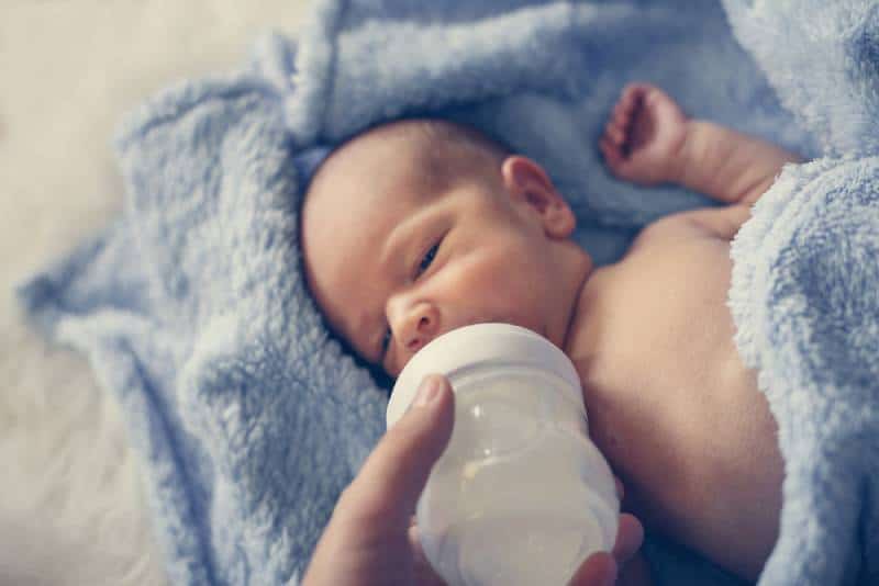 Mother feeding milk bottle to newborn baby boy.