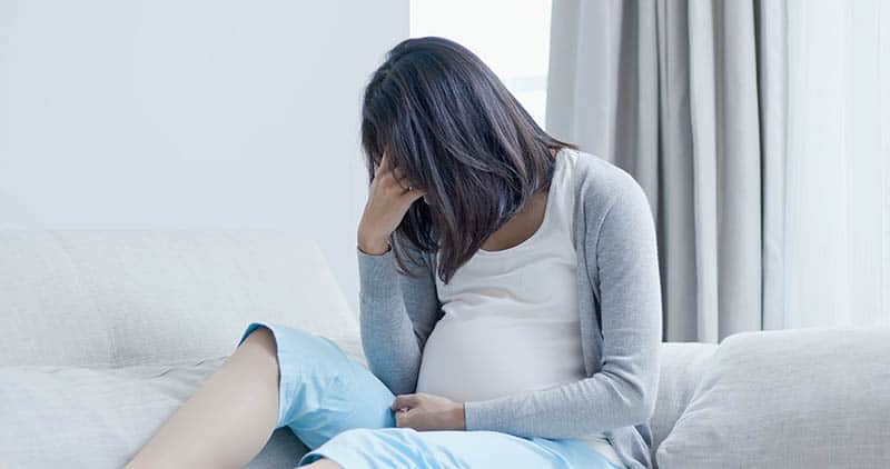 Pregnant woman in pain sitting on sofa 