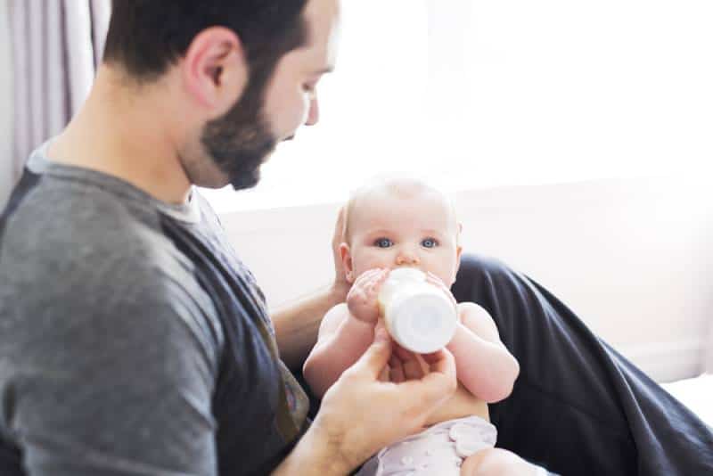father feeding milk to baby daughter