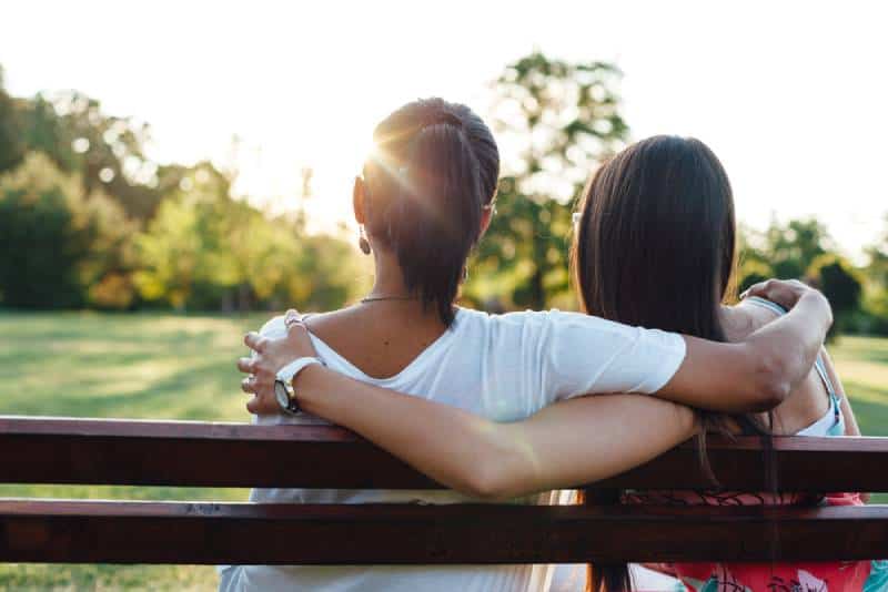 mom and daughter embracing on a park bench at sunset