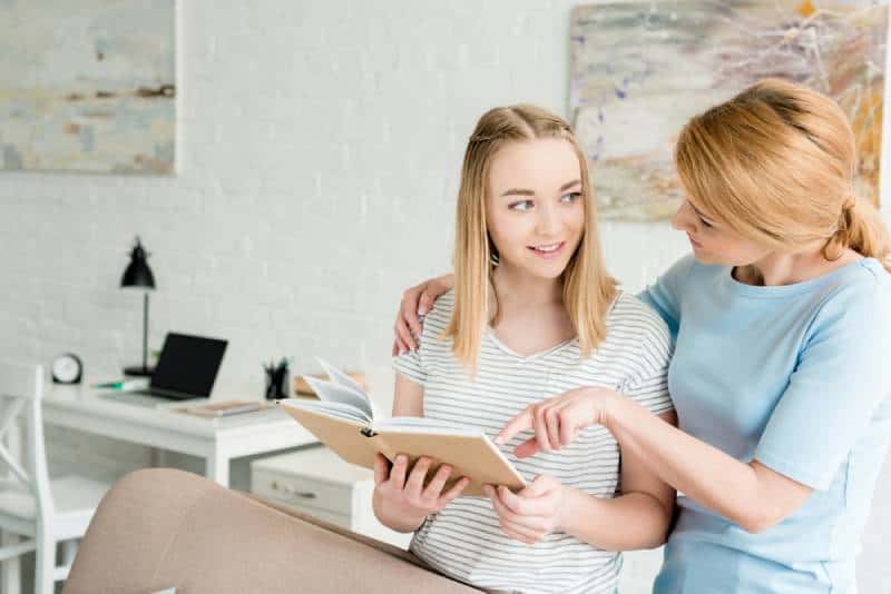 mother and teen daughter reading book together
