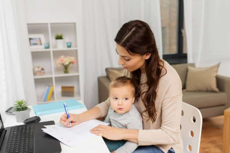 mother with baby, papers and laptop working at home