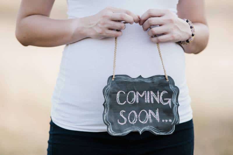 pregnant woman holding coming soon chalkboard sign