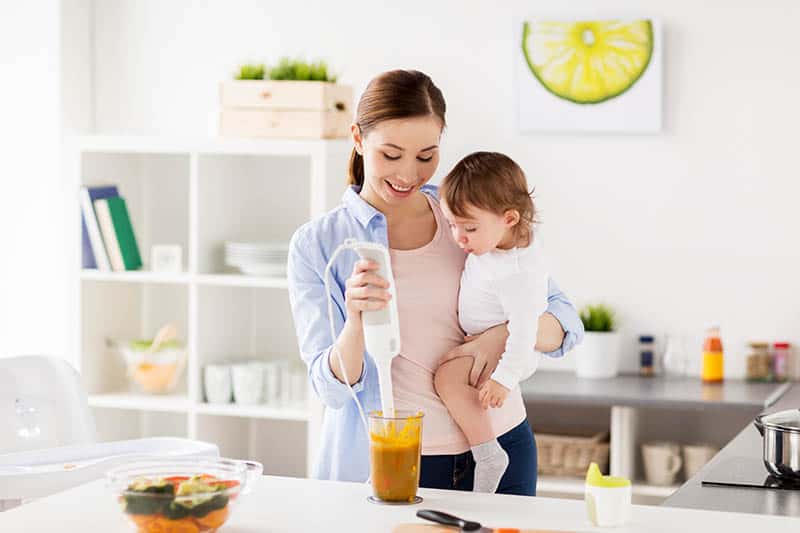 woman making baby food while holding baby in hand