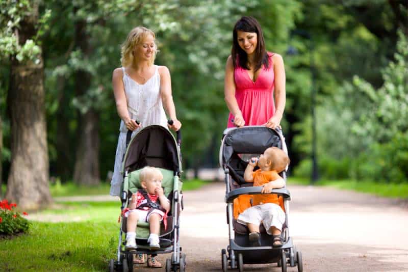 Happy mothers walking together with kids in strolles
