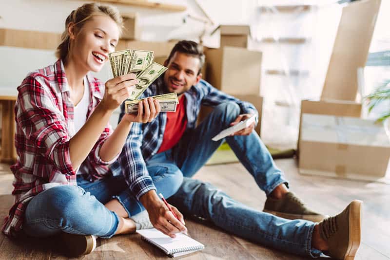 Couple sitting on the floor at home and looking happy for money they saved