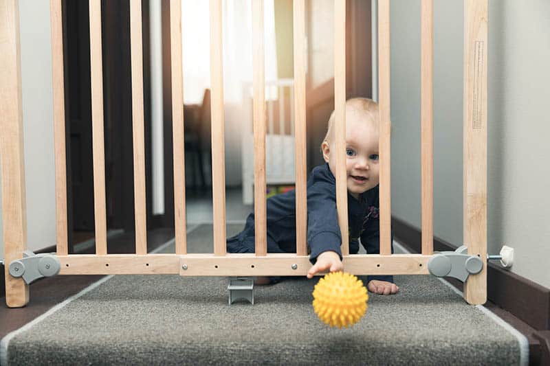 baby boy playing with ball behind baby gate