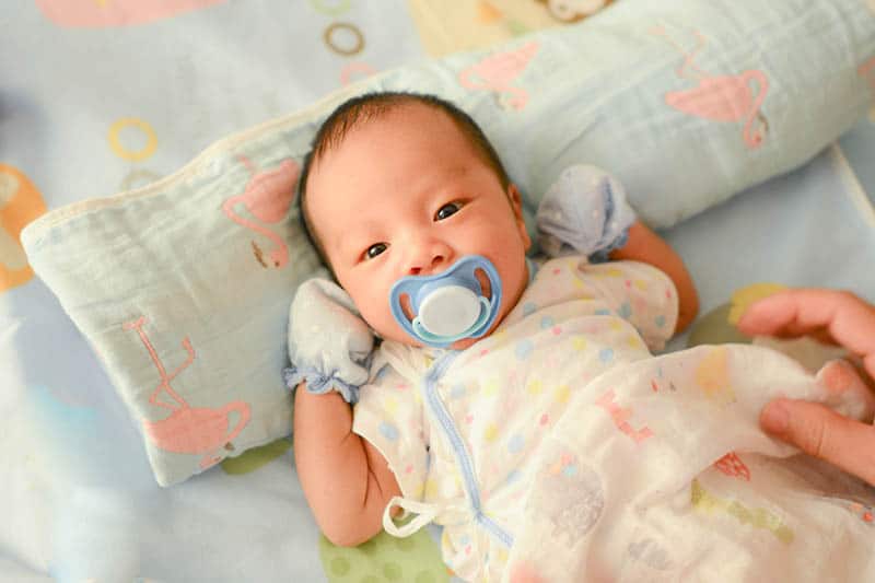 cute asian baby with pacifier lying in bed