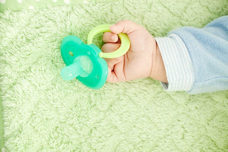 green pacifier in baby's hand