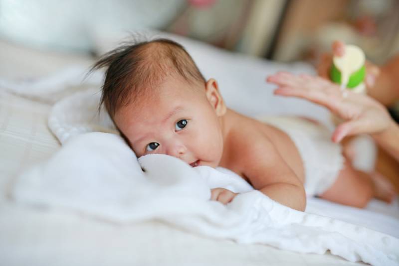 infant baby lying on the bed with mother hands applying a lotion cream
