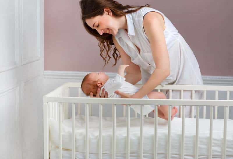 smiling mother putting baby in the crib