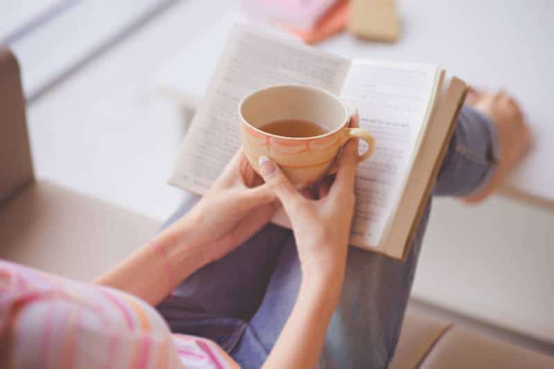 woman holding teacup in front of opened book and enjoying