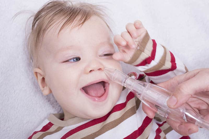 baby laughing while getting a nasal aspirator 