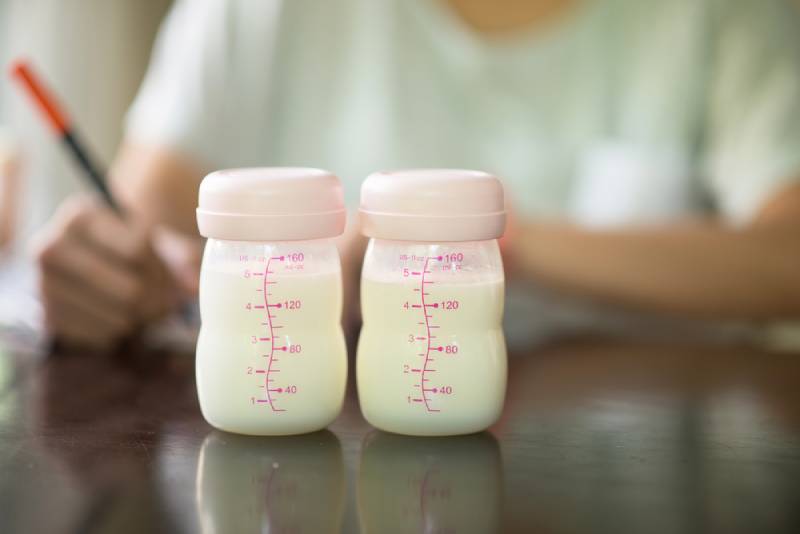 Two bottles of breast milk on table next to someone who is writing