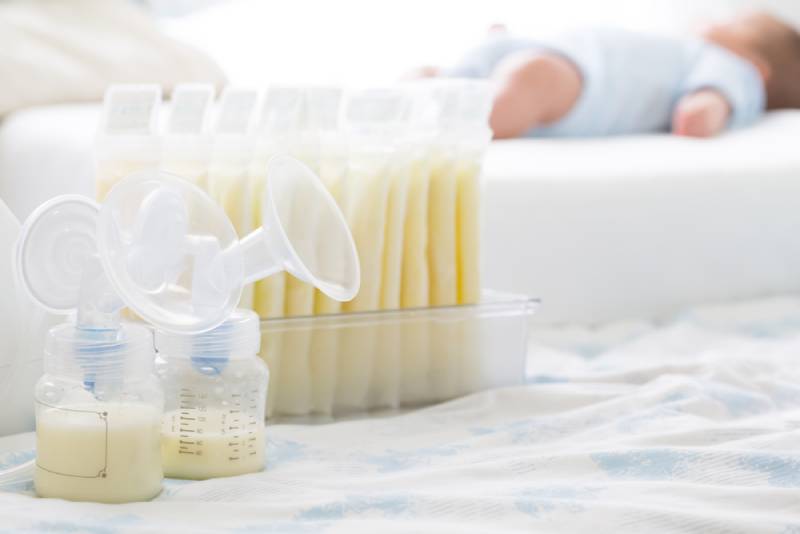 Breast milk frozen in storage bag and baby lying on bed