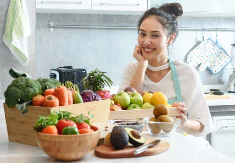 Woman in kitchen with various kind of vegetable and fruits