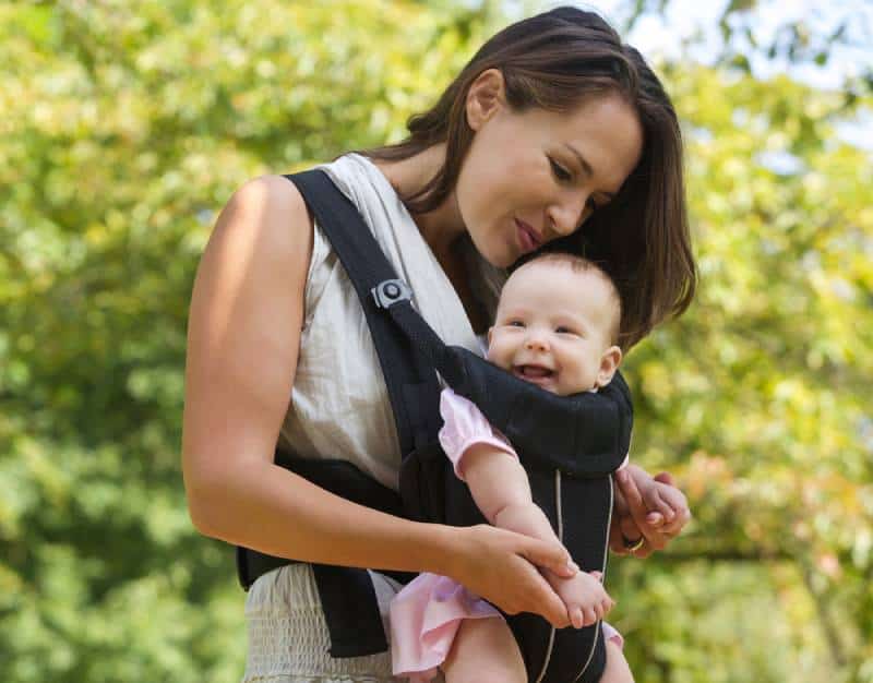 Happy mom with a baby in a carrier enjoying outdoors