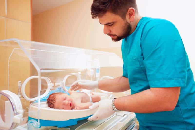 man taking care of newborn baby in infant incubator