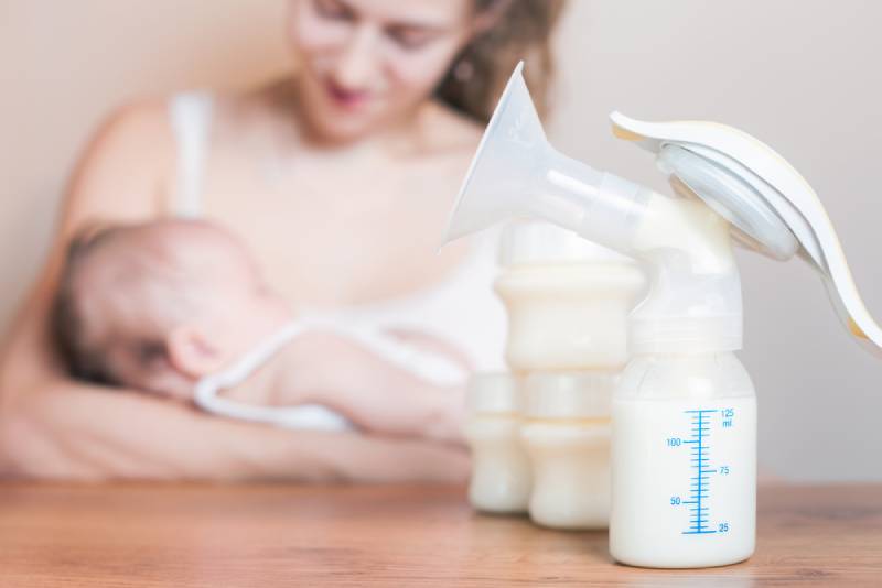 Mom holding a baby next to a breast pump