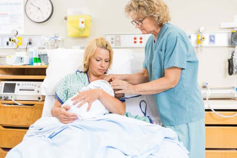 Woman in hospital is breastfeeding with some help of a midwife