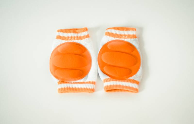 Orange knee pads for babies on light surface