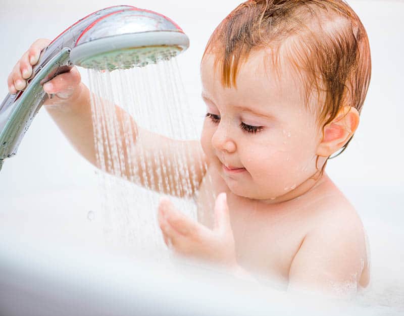 baby holding shower head during bath