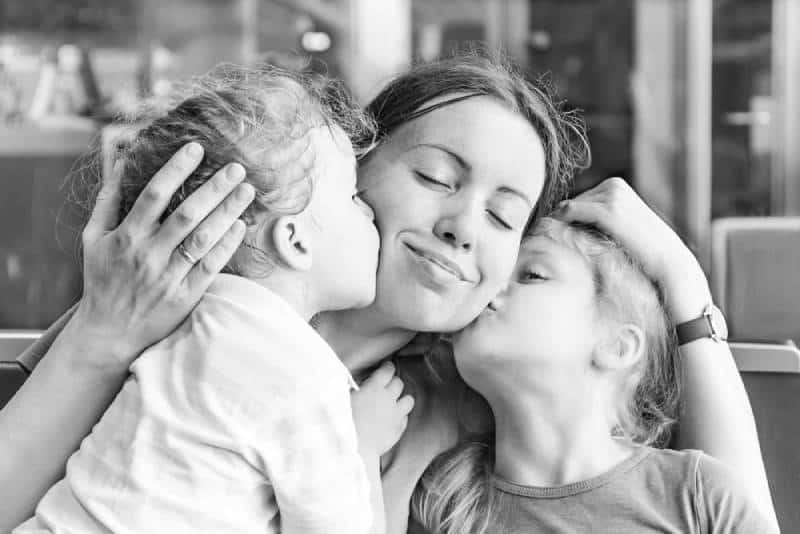 Two daughters kissing their happy mother indoors