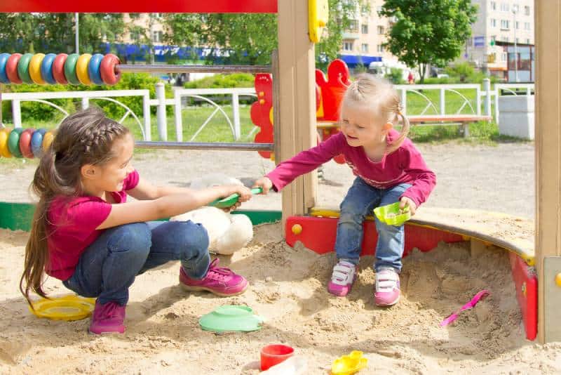 Two kids fighting over a toy shovel in the sandbox