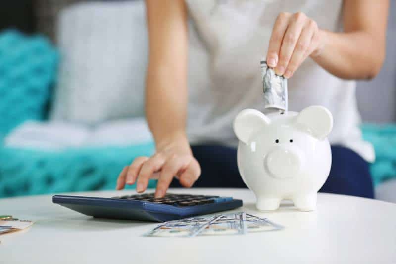 Woman putting money into piggy bank next to a calculator