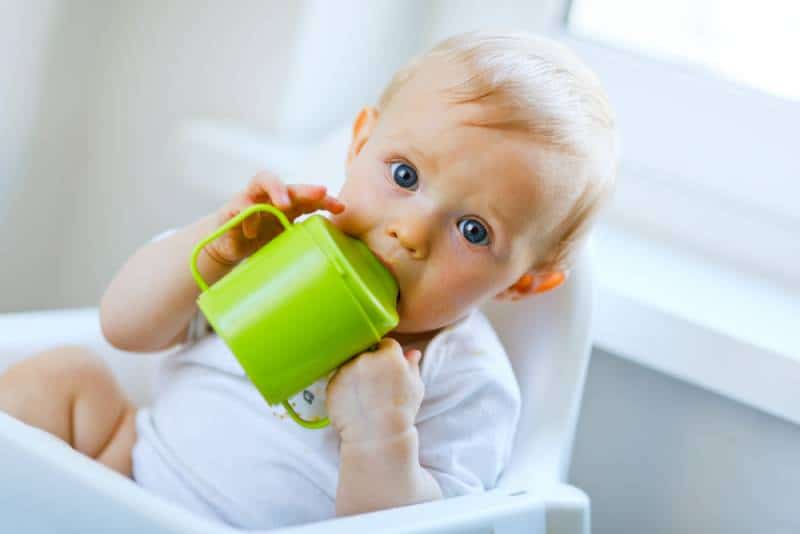 baby sitting in chair and drinking from baby cup