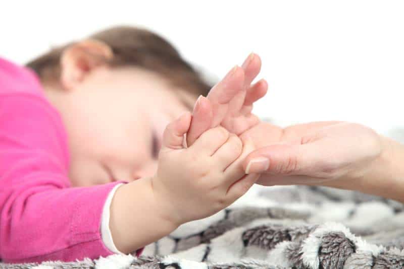 Baby sleeping takes the hand of her mother