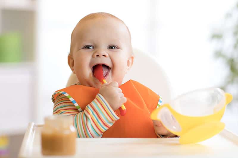 baby laughing while holding a spoonn