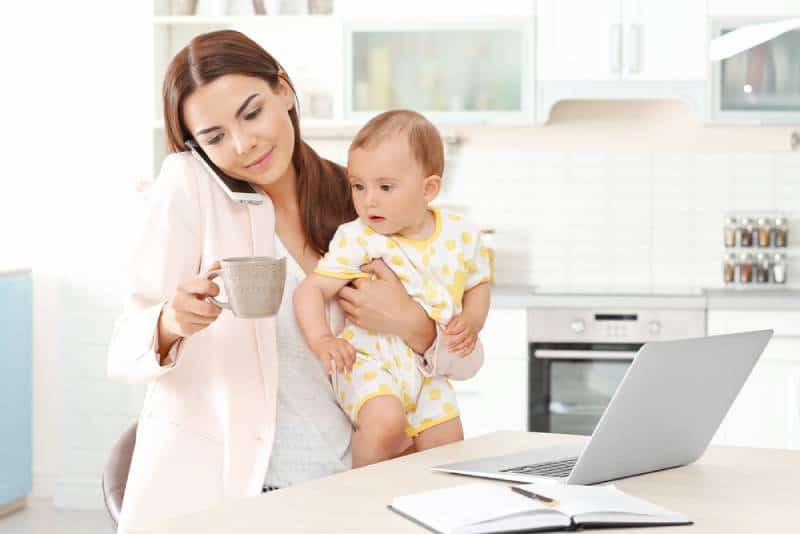 mother holding baby while talking on phone at home