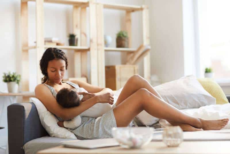 mom sitting on sofa bed and breastfeeding baby